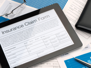 An iPad sits on a desk with an insurance claim form appearing on the screen.
